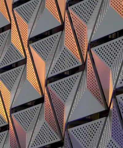Bild einer grauen Metallverkleidung an einem Gebäude mit Löchern, die ein interessantes Muster aus Licht und Schatten in dreieckigen Formen bilden