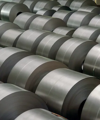 A large number of rolled steel coils stacked in rows inside an industrial warehouse.
