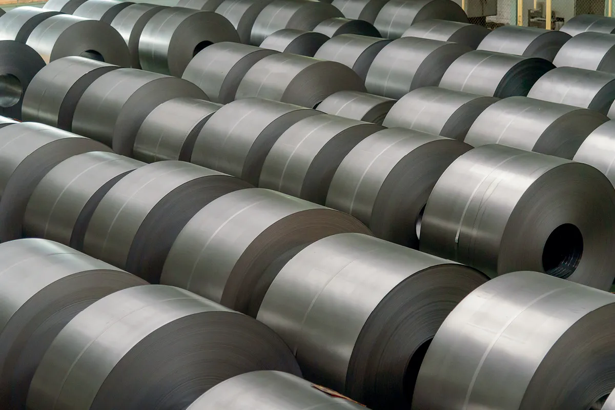 A large number of rolled steel coils stacked in rows inside an industrial warehouse.